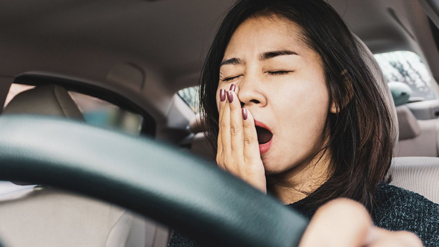 Tired woman yawning while driving car