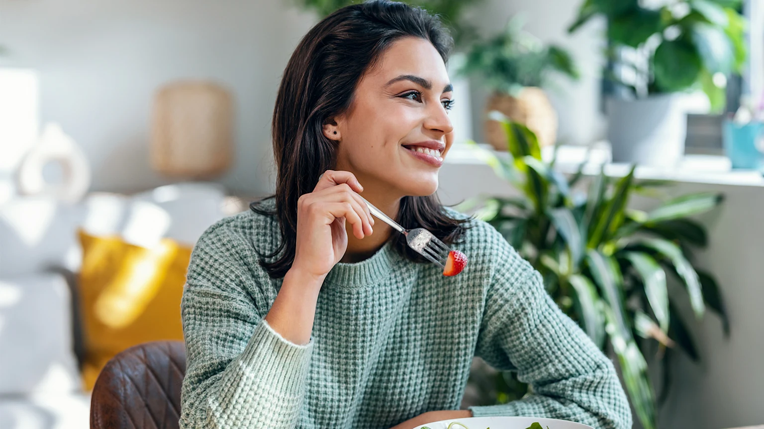 Woman eating fruit salad smiling and looking out the window