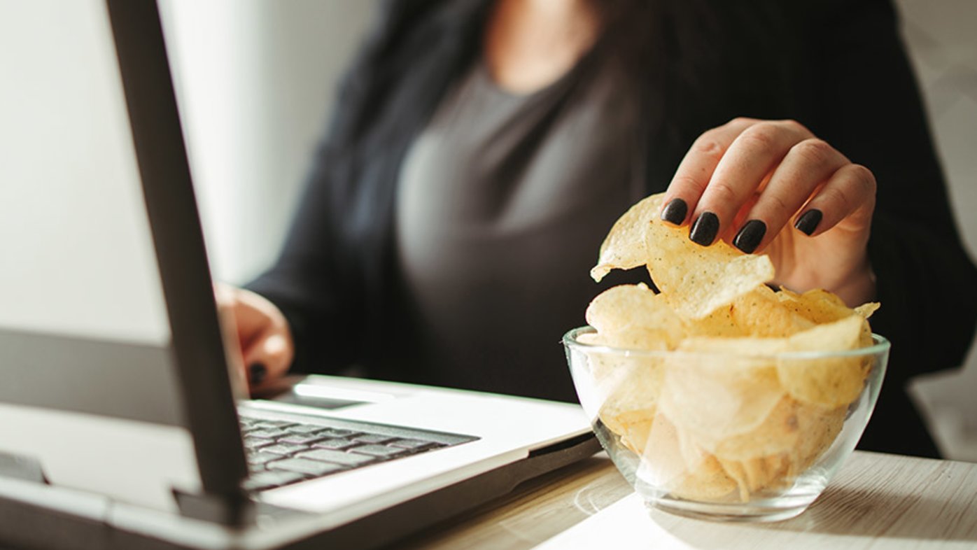 Woman eating potato chips while working on a laptop computer