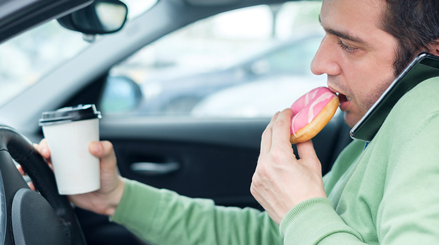 Man eating donut and talking on the phone while driving
