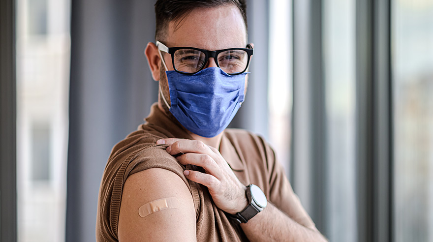 Man wearing face mask and showing vaccine bandage