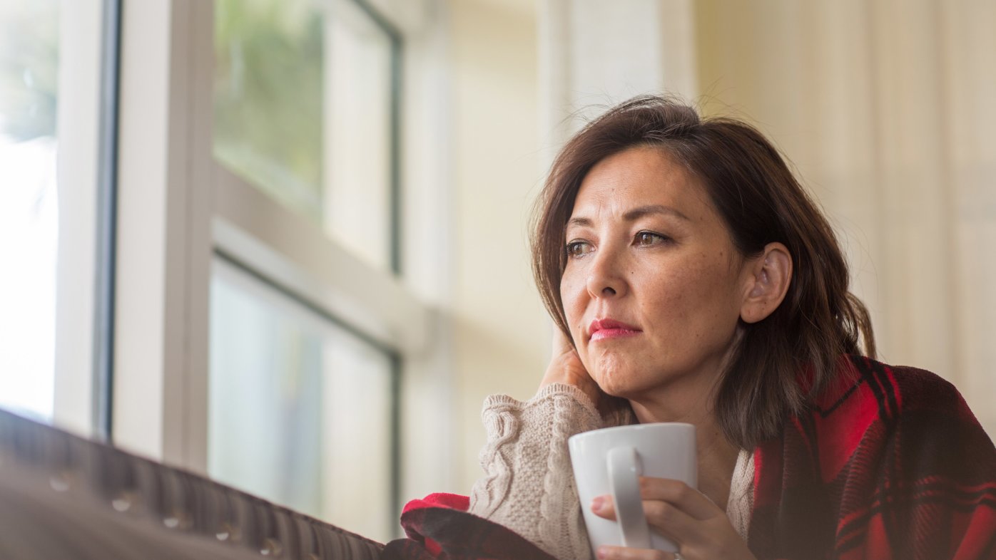 Woman with blanket and coffee looking out the window