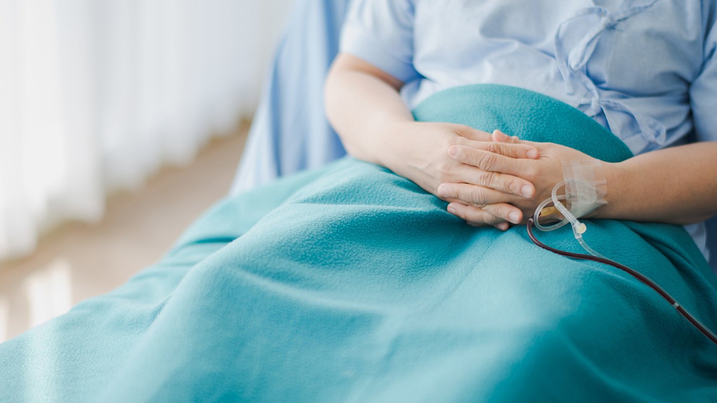 Person sitting in hospital bed with clasped hands and a blanket