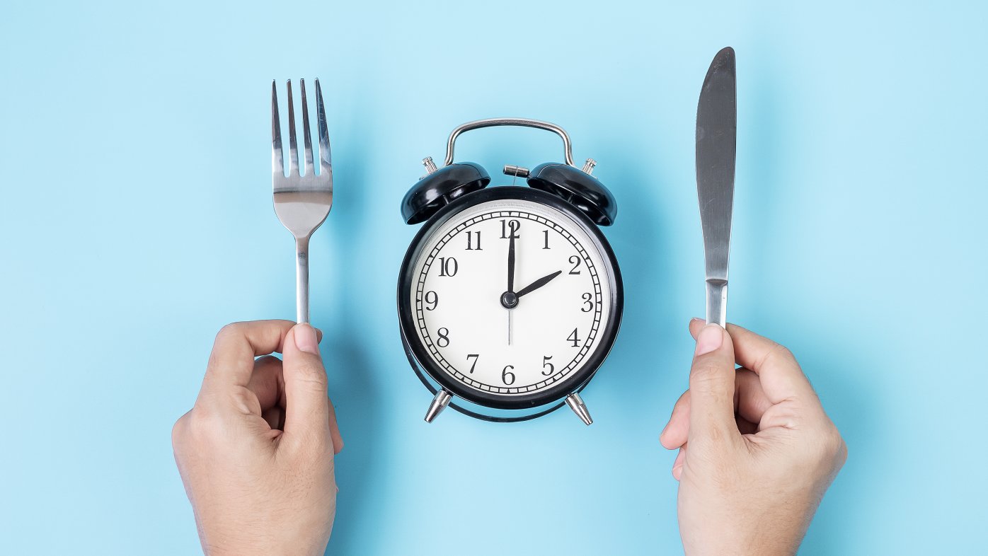 Person holding a knife and fork over an alarm clock
