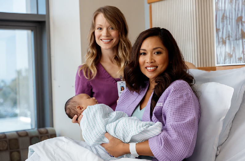 Mother in purple robe holding newborn with nurse in purple scrubs in back