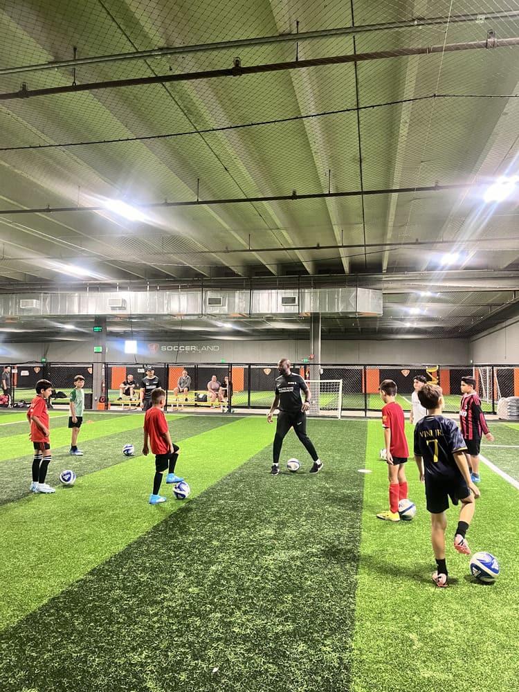 Friendly soccer coach supporting a child in training session.
