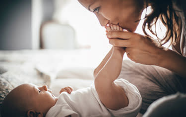 Frau küsst die Füße des neugeborenen Babys