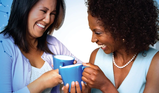 Two women smiling and talking while holding blue mugs.