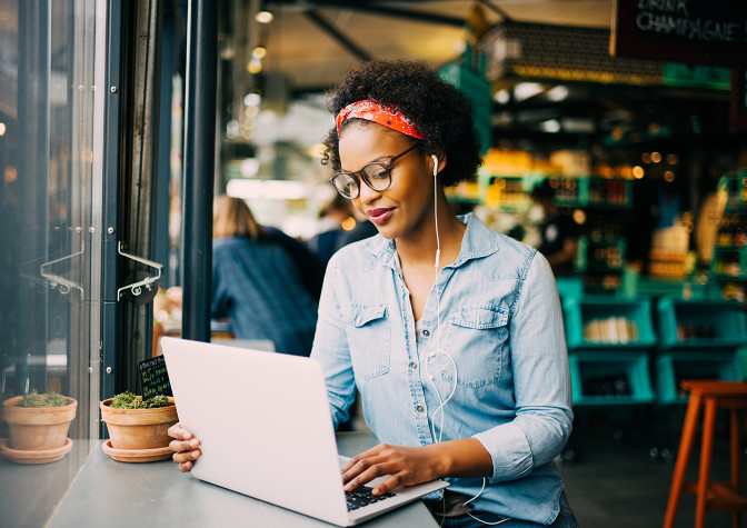 Woman in a coffee shop smiling while listening to music and using a laptop