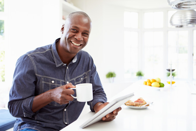 Man smiling drinking coffee reading tablet