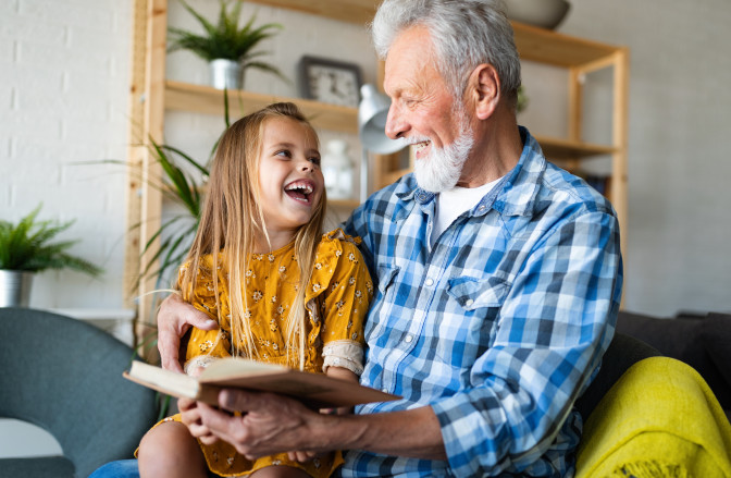 Grandpa reading a book to granddaughter laughing