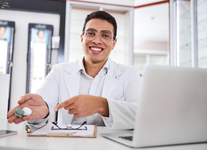 Eye Doctor near me smiling holding contact lense case sitting in desk, Contact Lens Eye Exam: What To Expect