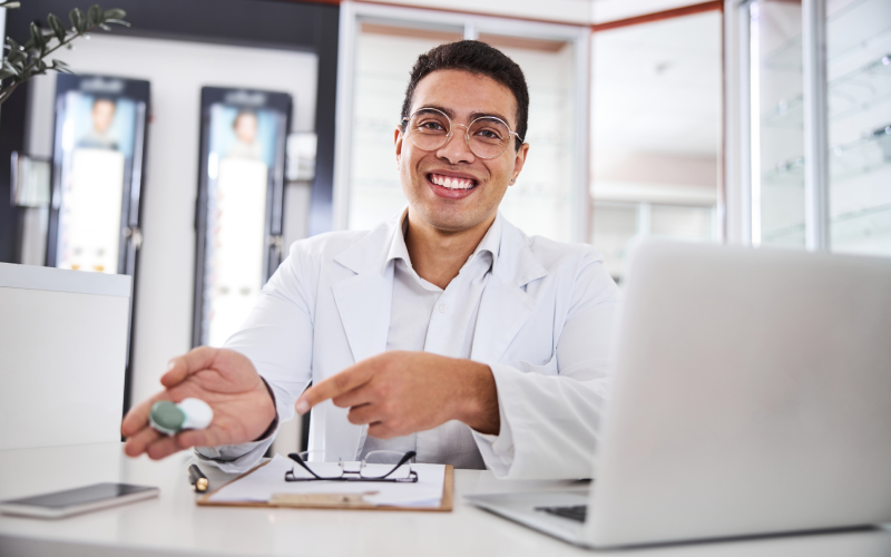 Eye Doctor near me smiling holding contact lense case sitting in desk, Contact Lens Eye Exam: What To Expect