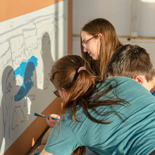 Students painting a mural on an interior wall together during a hands-on art activity.