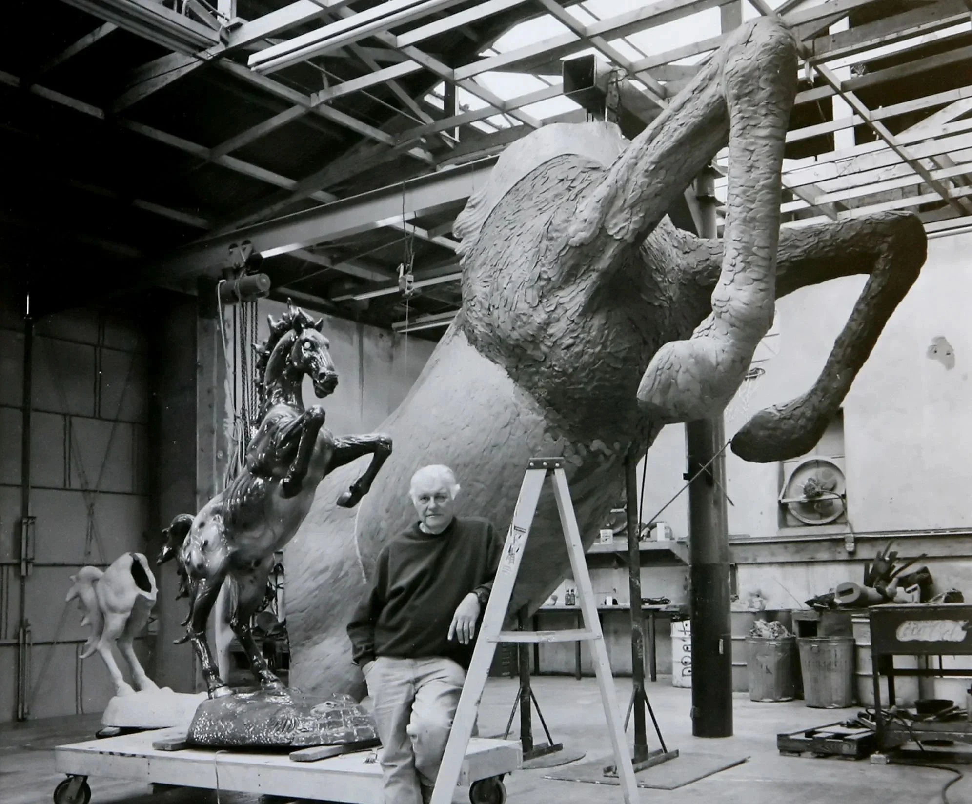 Man beside large horse sculptures in industrial workshop