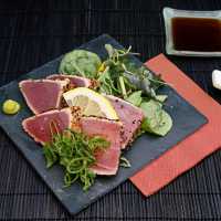 Fancy plate of seared ahi tuna salad on black dish, dark placemat and chopsticks, and bowl of soy sauce