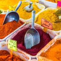 Open bins of colorful red, orange, yellow, and green spices with scoops and price tags
