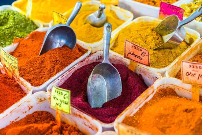 Open bins of colorful red, orange, yellow, and green spices with scoops and price tags