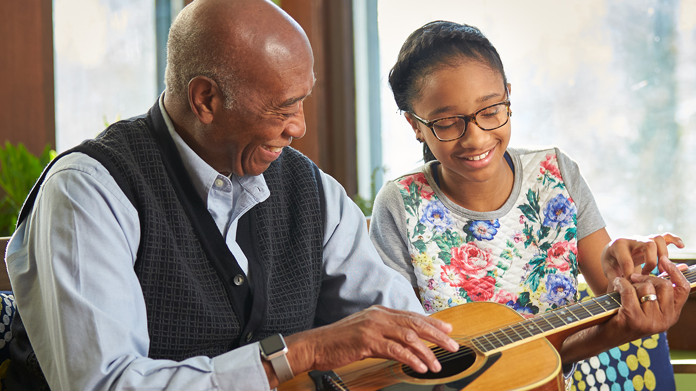 Elderly African American  man playing guitar with young African American girl both smiling.