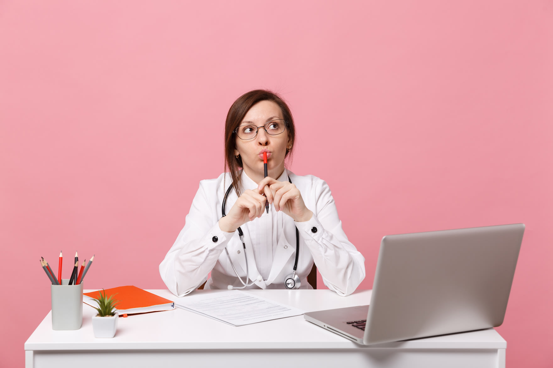 beautiful-female-doctor-sits-desk-works-computer-with-medical-document-hospital-isolated-pastel-pink-wall-background-woman-m