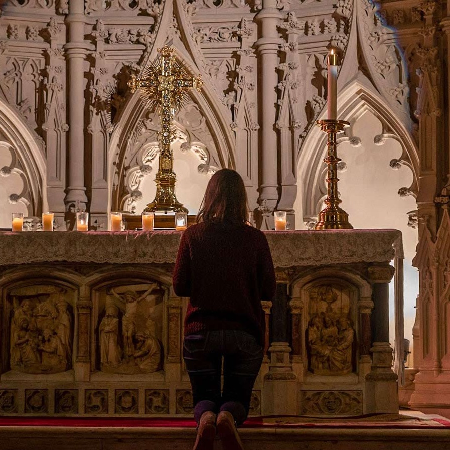Woman kneeling before ornate cross at an altar