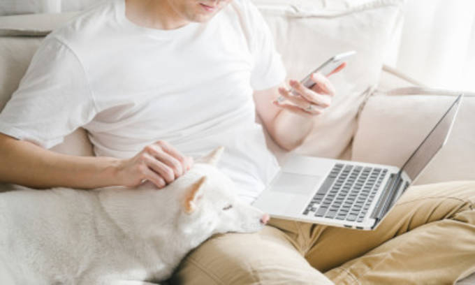 Un hombre se sienta en un sofá con un ordenador portátil en su pierna y un móvil en su mano.