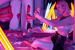 Girl taking a selfy surrounded by mirrors and office light bulbs in an purple room.