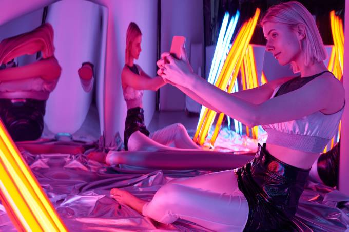 Girl taking a selfy surrounded by mirrors and office light bulbs in an purple room.