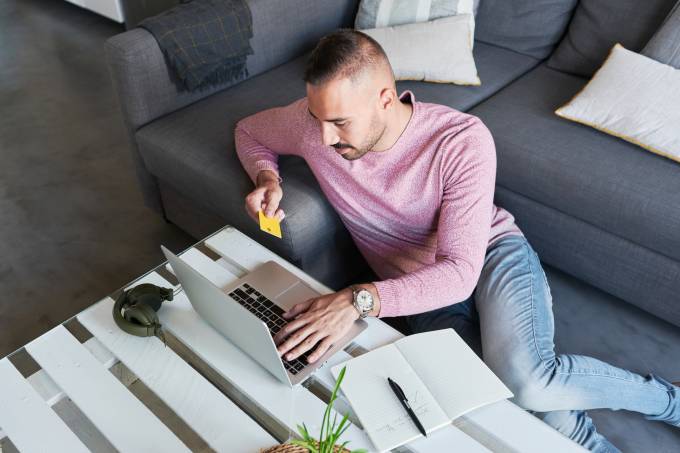 uomo seduto sul pavimento e lo shopping online con il suo computer portatile e carta di debito.