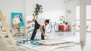 un artista freelance pintando en el suelo con color azul y naranja en una habitación muy blanca y luminosa.