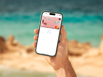 Una mano sostiene un smartphone al aire libre que muestra una Mastercard N26 digital rosa con tema de equipaje en la pantalla.