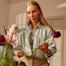 A woman with long blonde hair carefully trims a flower stem while arranging a bouquet.