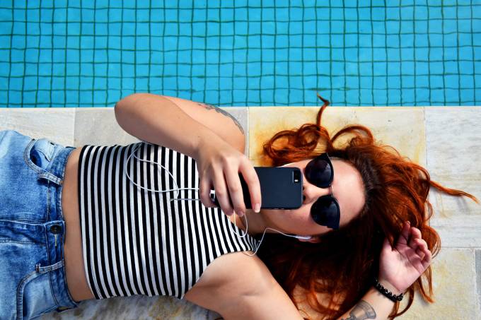 Woman lying on the boarder of a pool looking at her mobile.