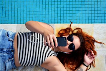Woman lying on the boarder of a pool looking at her mobile.