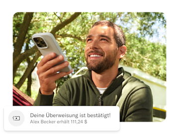 Mann hält sein Handy, unter ihm ist eine Push-Nachricht zu seiner Auslandsüberweisung zu sehen.