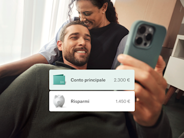 Una coppia è seduta sul divano, l'uomo sta guardando il suo telefono.