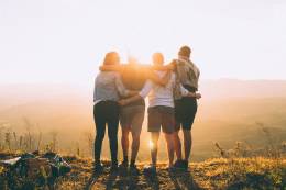 Un grupo de personas abrazadas al atardecer. 