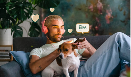 A man checking his smartphone on the sofa along with his dog.