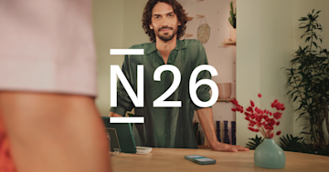 Un hombre sonriente está detrás de un mostrador con el gran logotipo de N26 superpuesto.