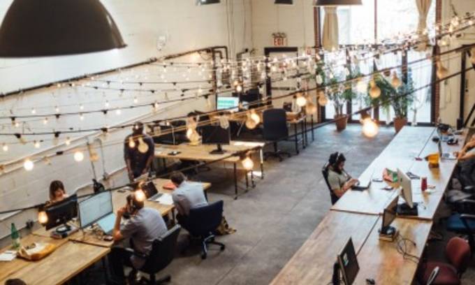 uno spazio di coworking con molti liberi professionisti seduti in una grande area aperta.