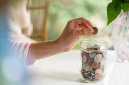 hand of a woman putting a coin in a glass jar.