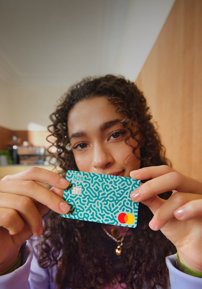 Dans un café moderne et lumineux, un adolescent tient devant son visage une carte de débit N26 à motifs turquoise réservée aux moins de 18 ans.