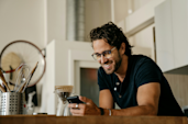 A man making coffee looks at his phone. 