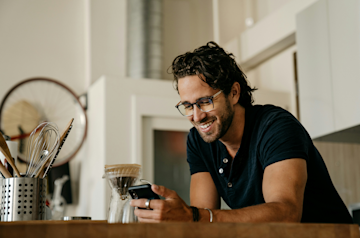 A man making coffee looks at his phone. 