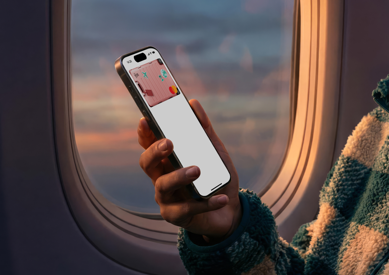 A person holds a smartphone displaying a digital N26 metal card in front of an airplane window showing a sunset sky.