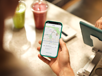 Eine Hand hält ein Smartphone, das die N26-Kartenoberfläche mit einem markierten 'CASH26'-Partnerstandort anzeigt.