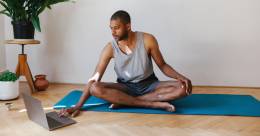 Person sitting on a yoga blanket preparing to exercise and searching for a workout in his computer.