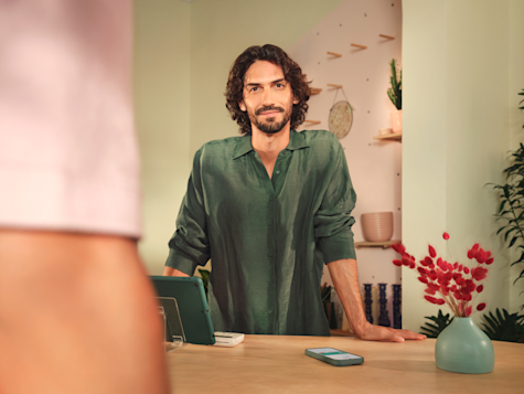 A smiling man in a dark green shirt stands behind a wooden counter in a store.