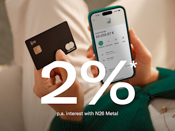 Woman dressed in blue, sitting, and holding her cell phone with the N26 application open. In the foreground, image of the 2% p.a. interest rate, balance in the main account, and in the savings account.