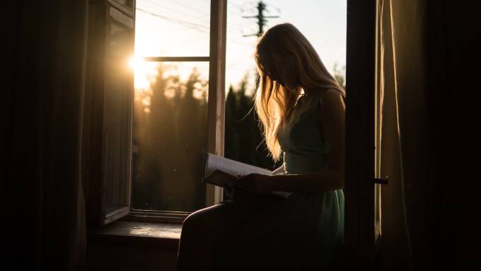 A woman reads a book by a window. 